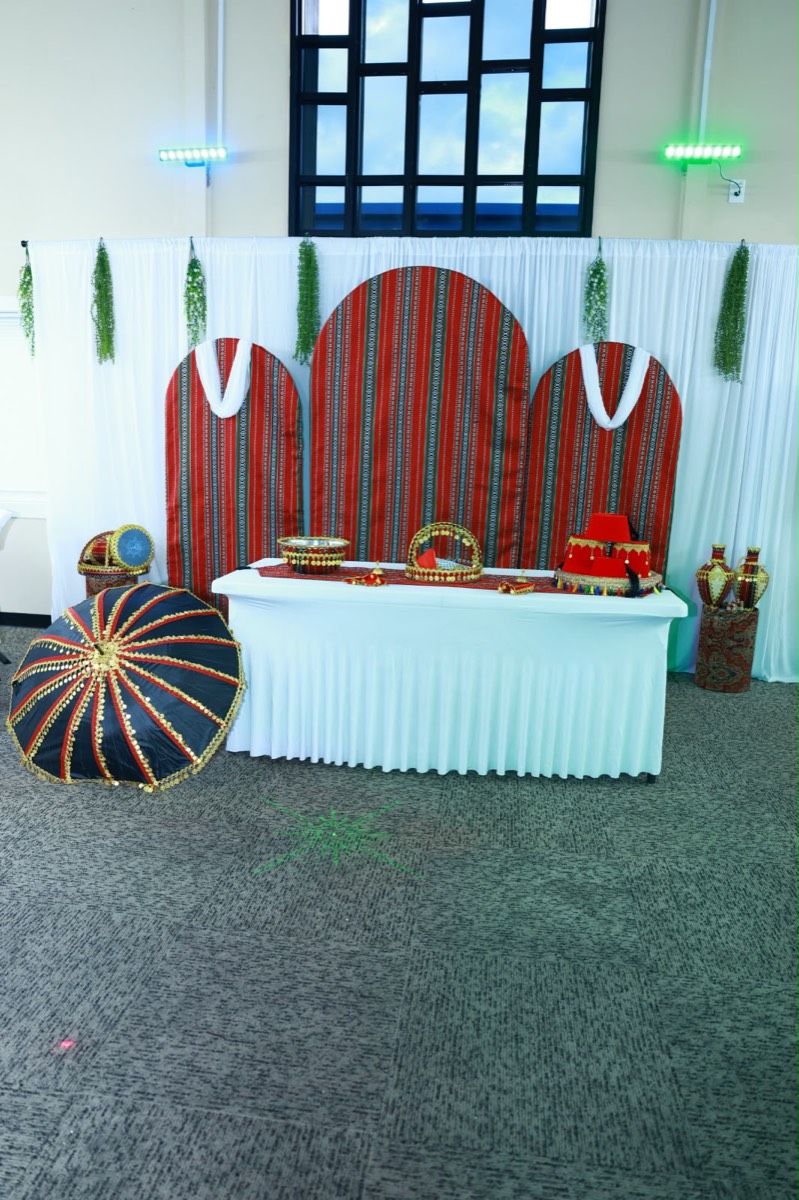 Traditional staging with red woven arched panels, gold serving trays and a coin-trimmed umbrella